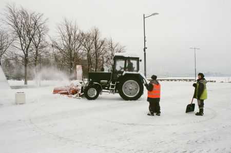 Workers with shovels and a tractore removing snow in a parking lot.