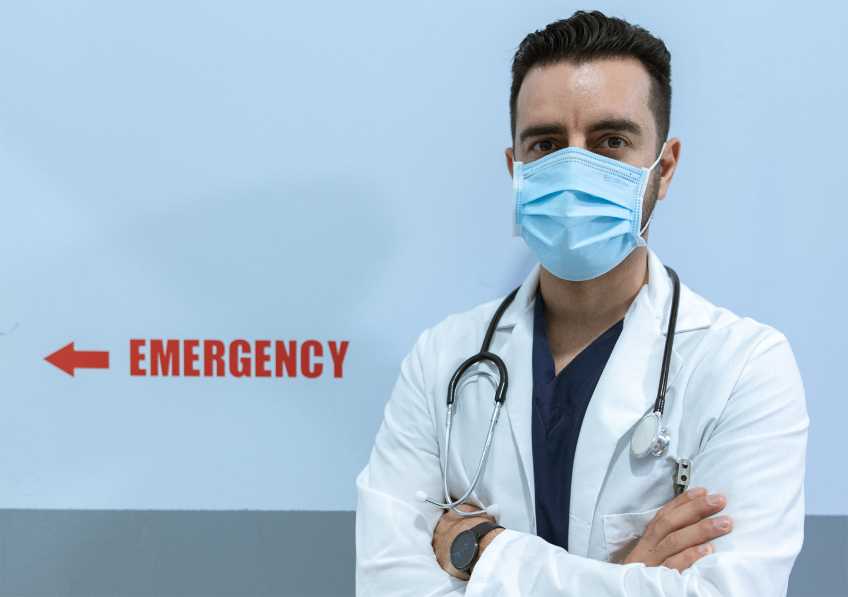Doctor standing in front of Emergency Room sign. 