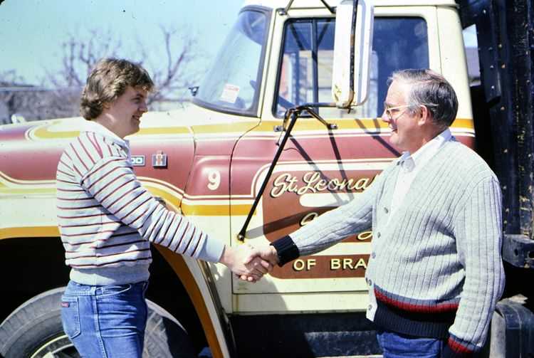 Historic photo of two men shaking hands in front of St. Leonard's truck