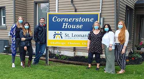 People in masks standing next to a Cornerstone House sign.