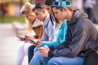 Group of young people sitting on a ledge looking at their phones.